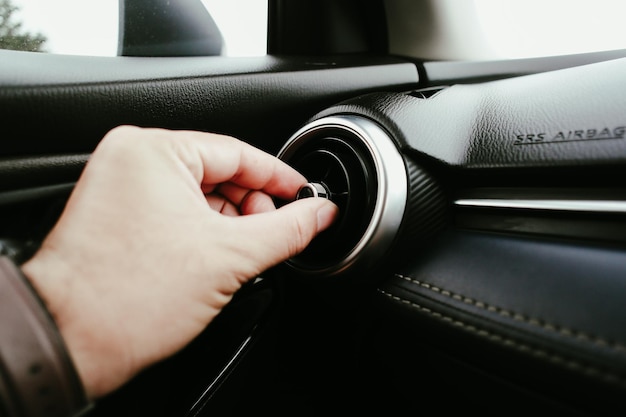 La mano del conductor ajusta la dirección del viento de la salida de aire en el automóvil. Ajuste de la dirección del botón del sistema de aire acondicionado en el automóvil. Concepto de aire acondicionado automotriz.