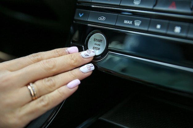 La mano del conductor femenino presiona el botón de arranque del motor de un automóvil