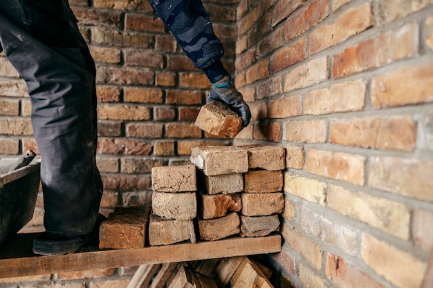 Mano de un constructor de casas tomando un ladrillo de una pila y haciendo una pared de ladrillos