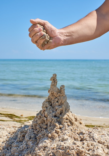 Foto la mano construye un castillo de la arena húmeda del mar.