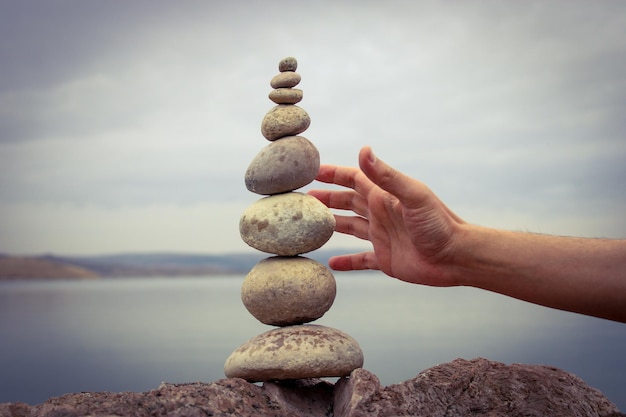 Una mano construye el equilibrio sobre guijarros. Equilibrio perfecto de pila de guijarros en la orilla del mar.