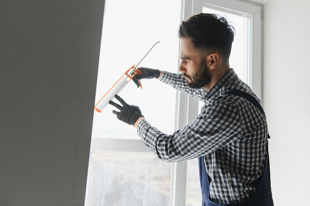 Mano de contratista sosteniendo una pistola de pegamento con silicona para reparar baldosas y ventanas Concepto de instalación o renovación de interiores