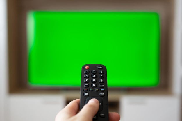 Una mano con un control remoto de tv sobre una pantalla verde un lugar para su publicidad