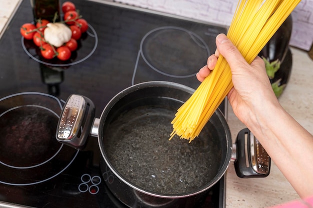 La mano de Cook deja caer los espaguetis en una cacerola con agua hirviendo.