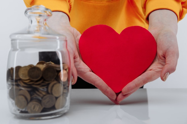 Foto mano con corazón y monedas en frasco de vidrio.