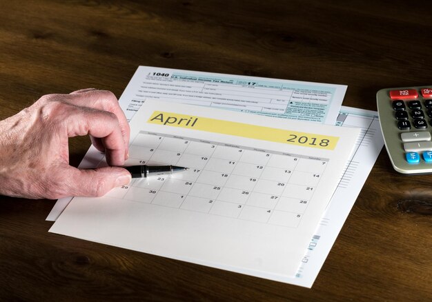 Mano cortada de un anciano con pluma y calendario en la mesa