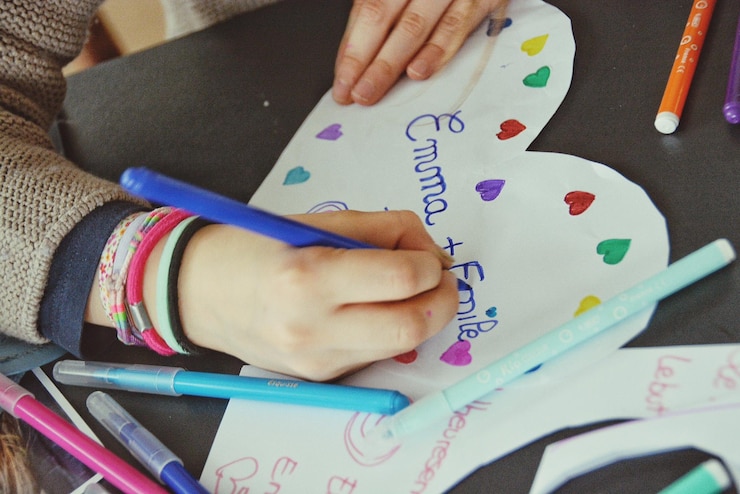 Foto mano cortada de una chica escribiendo en papel en forma de corazón en casa