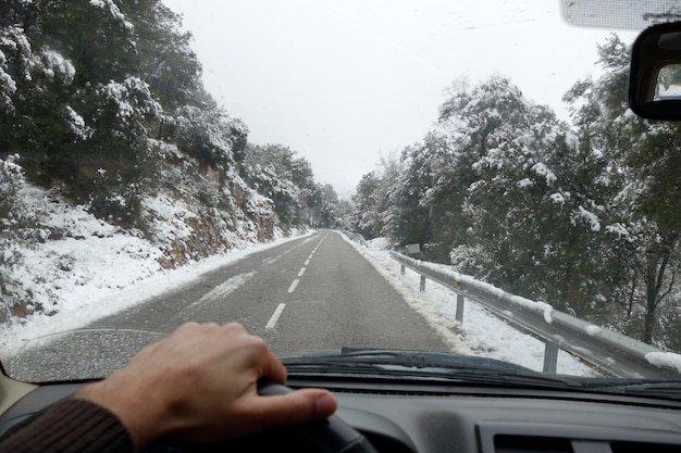 Foto mano cortada conduciendo un coche en la carretera durante el invierno