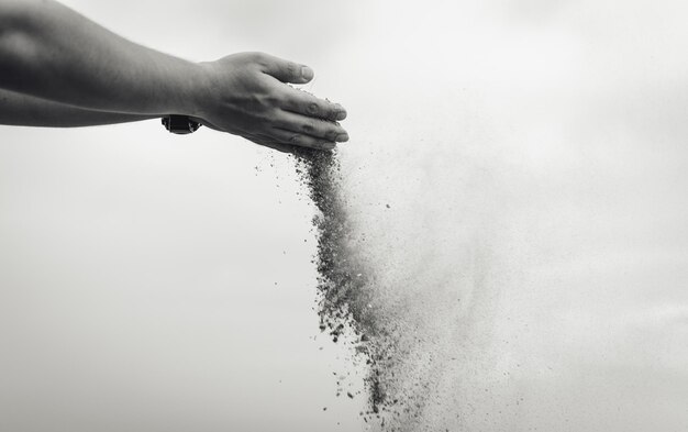 Foto la mano cortada esparciendo arena contra el cielo