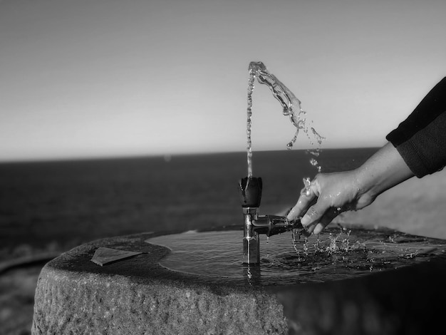 Foto mano cortada en la fuente de agua por el mar contra un cielo despejado