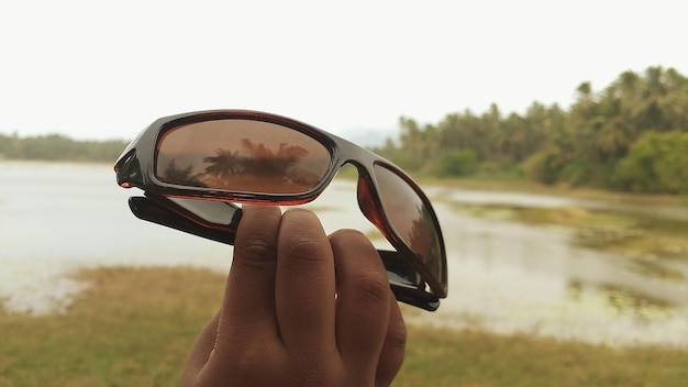 Foto mano cortada con gafas de sol junto al lago