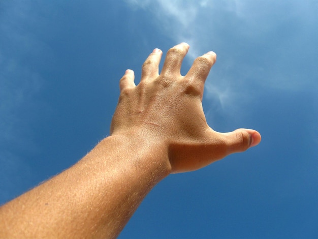 Mano cortada haciendo gestos contra el cielo azul
