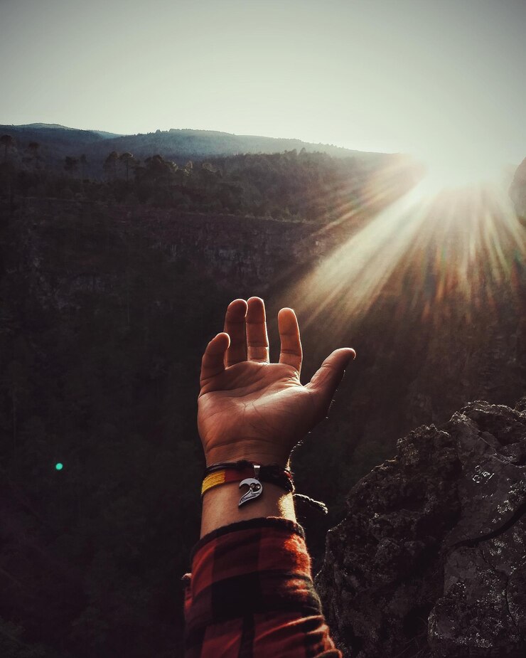 Foto mano cortada de un hombre gestando en la montaña hacia el cielo durante un día soleado