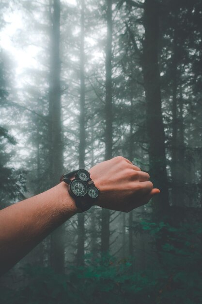 Mano cortada de un hombre que lleva un reloj de muñeca contra los árboles