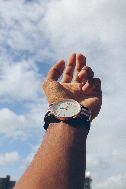 Foto mano cortada de un hombre que lleva un reloj de pulsera contra el cielo