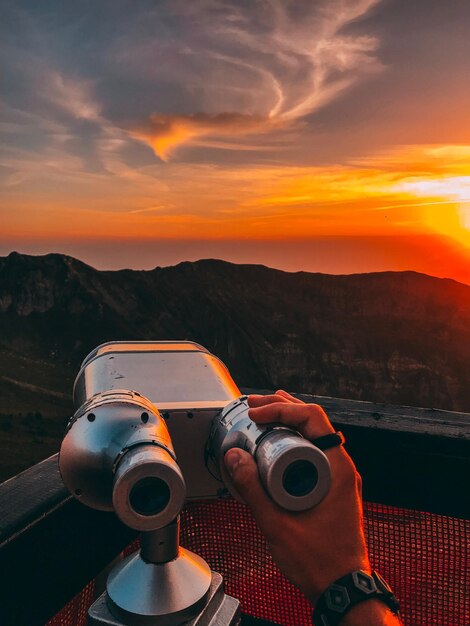 Foto mano cortada de un hombre sosteniendo un binocular con monedas contra el cielo durante la puesta de sol