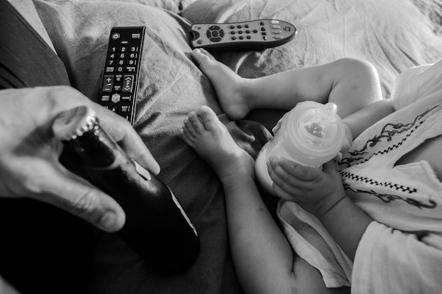 Mano cortada de un hombre sosteniendo una botella de bebida por un niño con una botela de leche en la cama