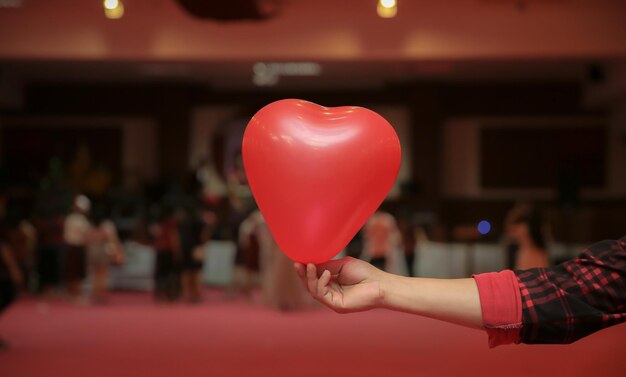 Foto mano cortada de un hombre sosteniendo un globo rojo en forma de corazón en una fiesta