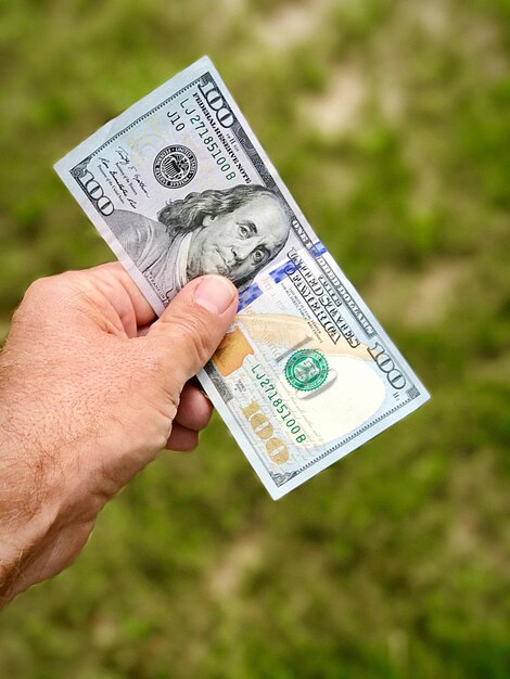 Foto mano cortada de un hombre sosteniendo papel moneda estadounidense sobre el campo