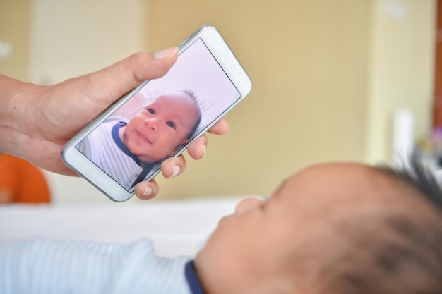 La mano cortada de la madre fotografiando a un bebé lindo en casa