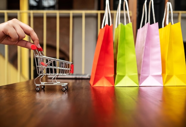 Mano cortada de una mujer con carrito de compras y bolsas en la mesa