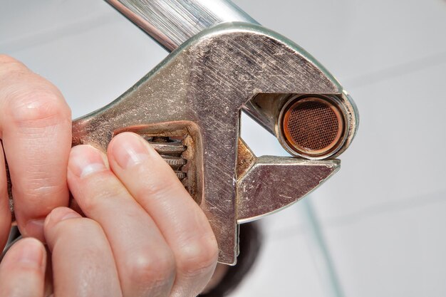 Foto mano cortada de una mujer desmontando un grifo con llave inglesa en casa