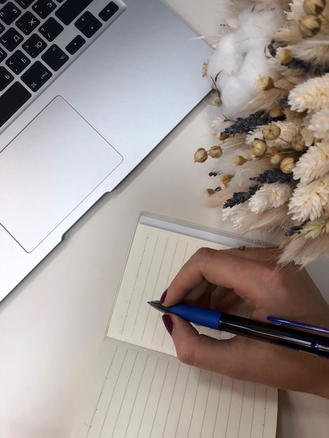 Foto mano cortada de una mujer escribiendo en un libro por una computadora portátil en la mesa