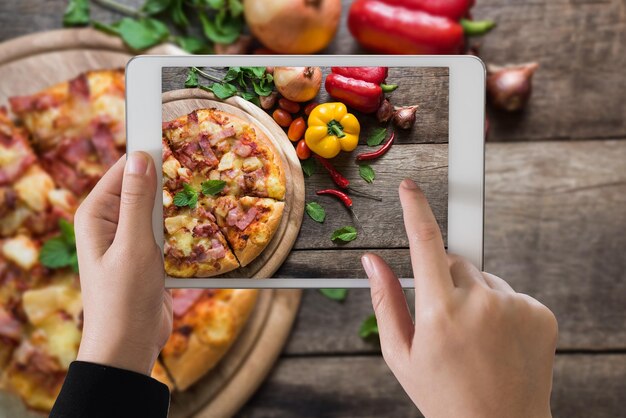 Mano cortada de una mujer fotografiando comida desde una tableta digital en la mesa