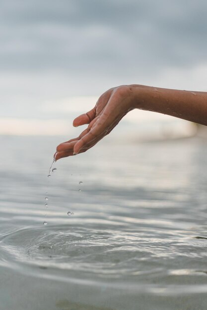 Foto mano cortada de una mujer jugando con agua en el mar