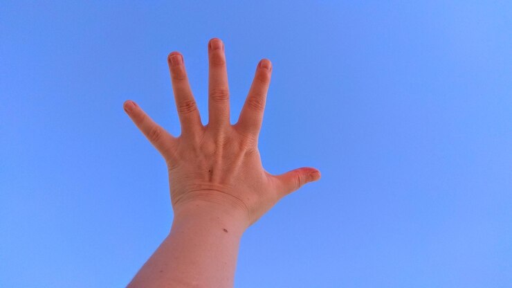 Foto la mano cortada de una mujer que se extiende contra el cielo azul claro