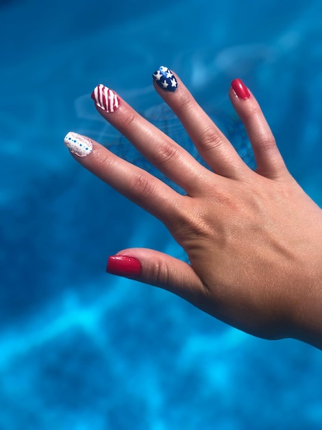 Mano cortada de una mujer que muestra pintura de uñas contra la piscina