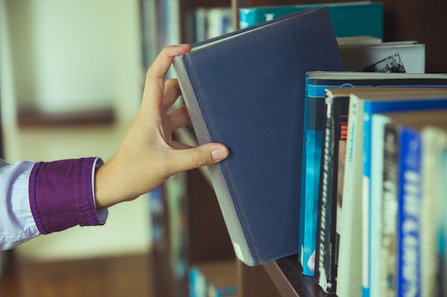 Foto la mano cortada de una mujer recogiendo un libro de la estantería