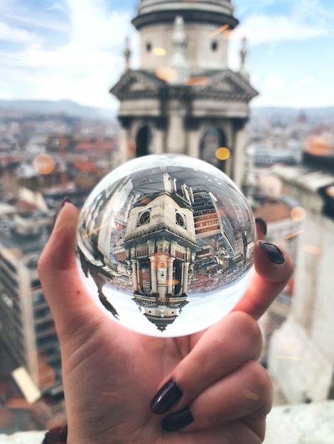 La mano cortada de una mujer sosteniendo una bola de cristal contra los edificios de la ciudad