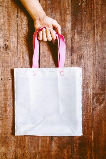 Mano cortada de una mujer sosteniendo una bolsa de compras contra la madera