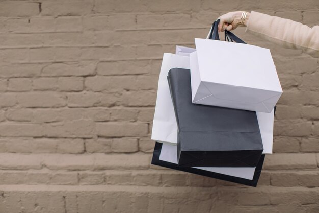 Foto mano cortada de una mujer sosteniendo bolsas de compras contra una pared de ladrillo