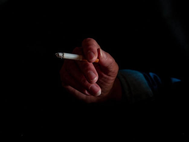 Foto mano cortada de una mujer sosteniendo un cigarrillo contra un fondo negro