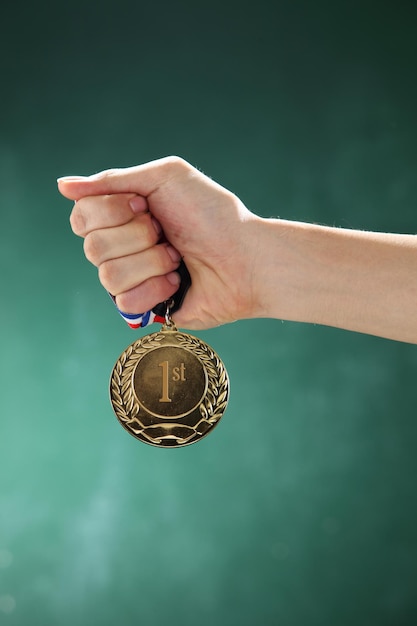 Foto la mano cortada de una mujer sosteniendo una medalla contra la pared