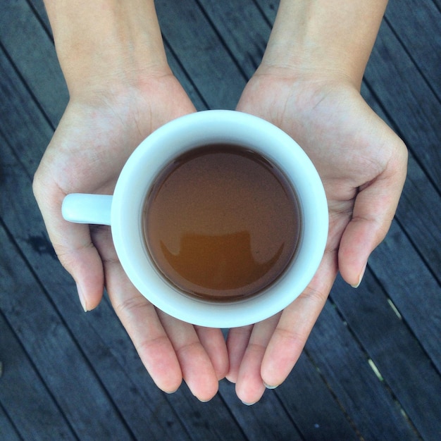 Mano cortada de una mujer sosteniendo una taza de té sobre el suelo de madera dura