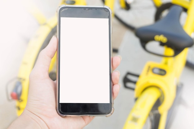 Foto la mano cortada de una mujer usando un teléfono en blanco contra bicicletas amarillas estacionadas al aire libre