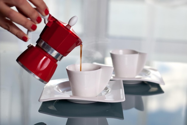 Mano cortada de una mujer vertiendo café en una taza en la mesa
