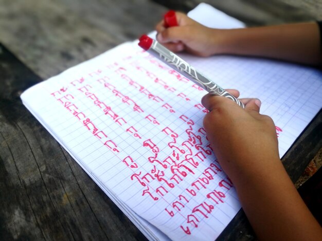 Mano cortada de un niño escribiendo en un libro en la mesa