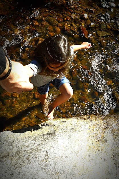 La mano cortada de un padre ayudando a su hija a escalar una roca junto al río