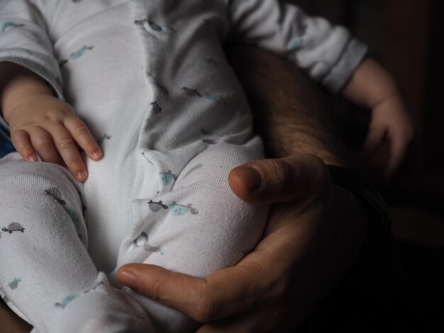 Foto mano cortada de un padre sosteniendo a su bebé en casa