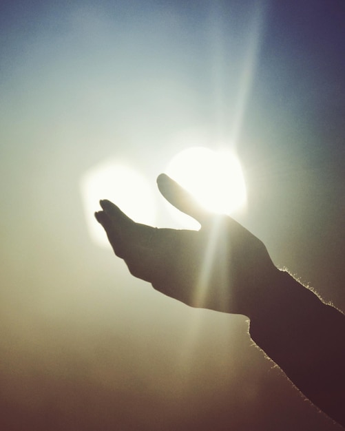 Mano cortada de una persona contra un cielo brillante