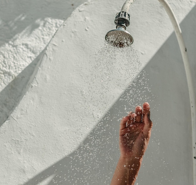 Mano cortada de una persona bajo la ducha con la cabeza contra la pared