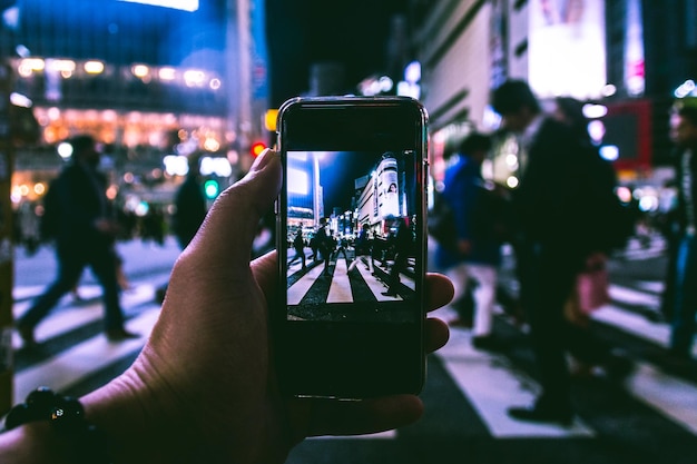 Mano cortada de una persona fotografiando a una multitud en un cruce de cebras por la noche