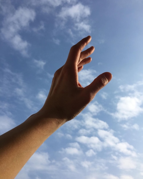 Foto mano cortada de una persona haciendo gestos contra el cielo