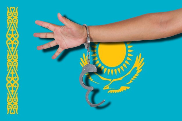 Mano cortada de una persona que lleva esposas contra la bandera de Kazajstán