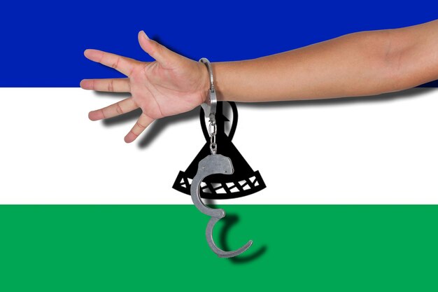 Mano cortada de una persona que lleva esposas contra la bandera de Lesotho