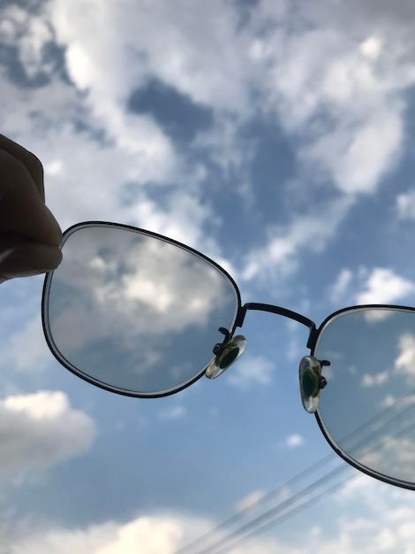 Foto mano cortada de una persona que sostiene gafas contra el cielo